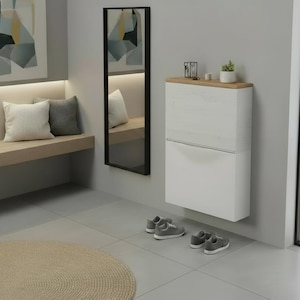 Könnte beinhalten: Ein moderner Eingangsbereich mit einem weißen Schuhschrank, einem langen Spiegel und einer Holzbank mit Kissen. Zwei Paar graue Turnschuhe stehen auf dem Boden. Ein runder beiger Teppich befindet sich im Vordergrund. Die Wände sind grau.