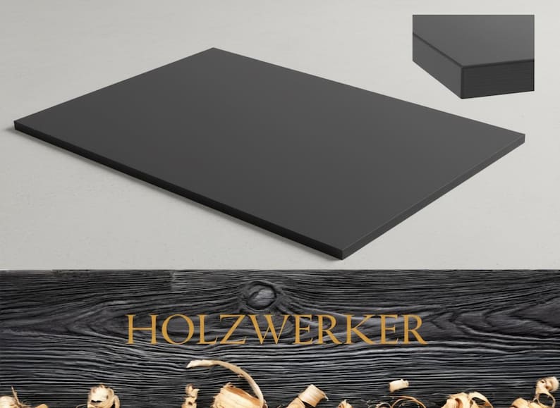 May include: A rectangular, matte black wooden board. The board is displayed on a light gray surface, with a close-up of the edge in the upper right corner. The word "HOLZWERKER" is displayed in gold lettering on a dark wood background.