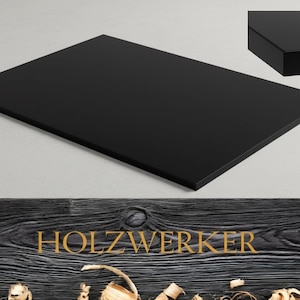 Könnte beinhalten: Eine rechteckige, schwarze Holz-Tischplatte mit glänzendem Finish. Das Bild enthält eine Nahaufnahme der Kante, die die Dicke zeigt. Das Wort "HOLZWERKER" wird in goldfarbenen Buchstaben auf einem Holzgrund angezeigt.
