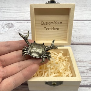 May include: A bronze crab figurine is held in front of an open wooden box filled with shredded paper. The box has a hinged lid and the text "Custom Your Text Here" is printed inside the lid.
