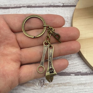 May include: A bronze-toned keyring with a large circular ring, a small chain, and two miniature wrench charms. One charm is a closed-end wrench with the number "1925", the other is an adjustable wrench with the text "Snap-on".