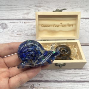 Könnte beinhalten: Eine blau-weiße Schneckenfigur aus Edelstein mit einer Holzbox. Auf dem Deckel der Box steht der Text "Custom Your Text Here". Eine weitere Schneckenfigur befindet sich in der Box.