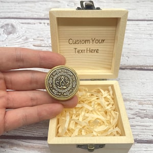 May include: A small, open wooden box with the text "Custom Your Text Here" engraved inside. A round, bronze-colored coin with a lotus flower design is held near the box. The box is filled with shredded paper.