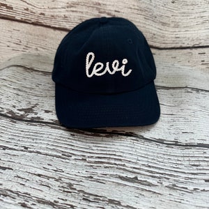 May include: A black baseball cap with a white embroidered cursive word "Levi" on the front.