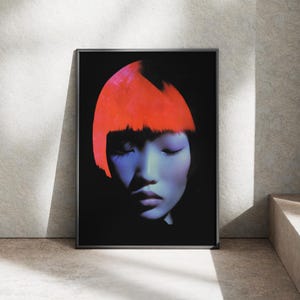 Könnte beinhalten: Gerahmter Kunstdruck mit einem Porträt einer Person mit geschlossenen Augen. Die Haut hat einen kühlen Blauton, kontrastiert durch leuchtend rotes Haar. Der Hintergrund ist schwarz, was den Farbkontrast verstärkt.