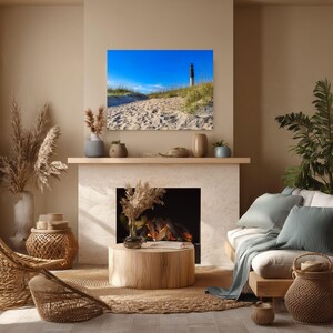 Peut inclure: Un salon sur le th&egrave;me c&ocirc;tier avec un tableau encadr&eacute; d'un phare sur un sentier sablonneux sous un ciel bleu. La pi&egrave;ce comprend une chaise en osier, une table basse en bois et une palette de couleurs neutres avec des plantes et des coussins d&eacute;coratifs.