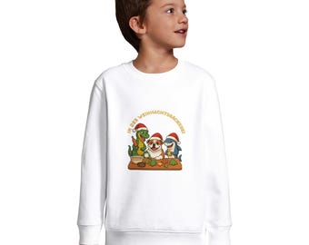 May include: White sweatshirt featuring a cartoon illustration of a dinosaur, dog, and shark wearing Santa hats and baking cookies. The text "IN DER WEIHNACHTSBÄCKEREI" is printed above the characters in gold.