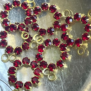 May include: Close-up of several gold-toned metal jewelry components, each featuring a circle of vibrant red gemstones. The gemstones are set closely together, creating a continuous line of color. The components have small loops for attachment.
