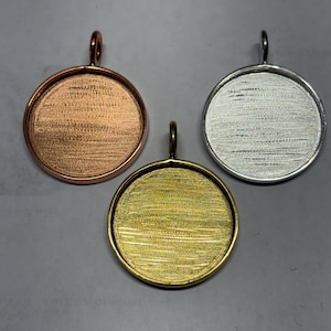 May include: Three circular pendant trays with a textured, brushed metal finish. One tray is copper-colored, one is gold-colored, and one is silver-colored. Each pendant tray features a small, vertical loop at the top for attachment to a chain.