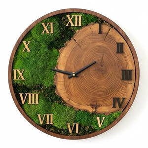 Op de afbeelding: Ronde houten wandklok met een natuurlijk houtnerfcentrum en een rand van groen mos. De klok heeft Romeinse cijfers en zwarte wijzers. Een decoratief item voor in huis.