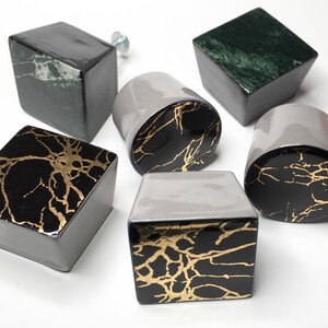 May include: Six ceramic cabinet knobs with a marbleised design. The knobs are in various shapes, including square and round. Some of the knobs have a black and gold marbleised design, while others have a green and white marbleised design.