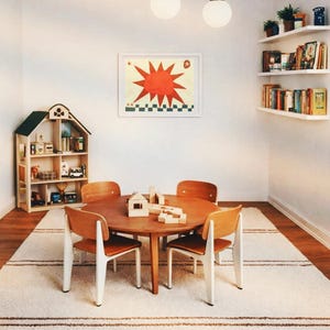 Peut inclure: Une salle de jeux pour enfants avec une table ronde en bois et quatre chaises. Une &oelig;uvre d'art encadr&eacute;e avec un soleil rouge est accroch&eacute;e au mur. Une maison de poup&eacute;e et des &eacute;tag&egrave;res avec des livres et des plantes compl&egrave;tent la sc&egrave;ne.