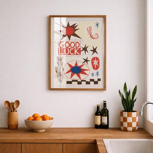 Puede incluir: Una l&aacute;mina de arte mural enmarcada con el texto GOOD LUCK en letras rojas. El dise&ntilde;o incluye un sol rojo, un escorpi&oacute;n, un pez, estrellas y un patr&oacute;n de cuadros en colores rojo, azul, negro y crema, todo dentro de un marco de madera.