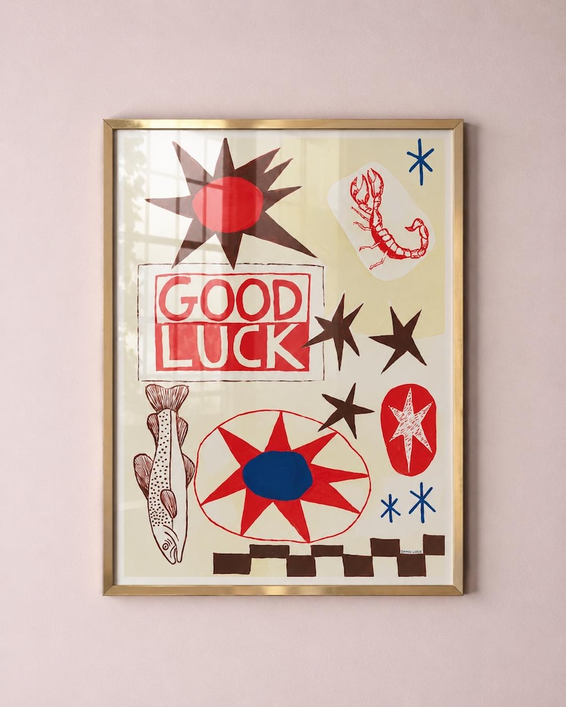 Puede incluir: Una l&aacute;mina art&iacute;stica enmarcada con fondo crema y el texto rojo GOOD LUCK dentro de un borde rectangular. El dise&ntilde;o incluye un escorpi&oacute;n rojo, un pez, un sol marr&oacute;n oscuro, una estrella roja y azul, y un patr&oacute;n de cuadros marr&oacute;n oscuro.