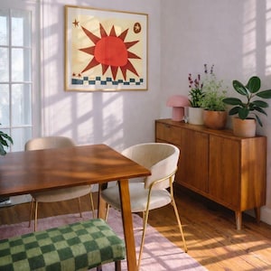 Peut inclure: Int&eacute;rieur de salle &agrave; manger avec une table en bois, des chaises et un banc &agrave; carreaux verts. Une &oelig;uvre d'art encadr&eacute;e avec un soleil rouge est accroch&eacute;e au mur. Un tapis rose et un meuble en bois avec des plantes et une lampe rose.
