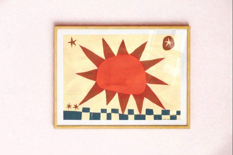 Peut inclure: Impression d'art encadr&eacute;e repr&eacute;sentant un soleil stylis&eacute; avec des rayons rouges et un cercle central rouge. L'&oelig;uvre comprend des &eacute;toiles et un motif &agrave; carreaux bleu et blanc en bas. L'impression est dans un cadre en bois.