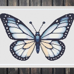 May include: A framed cross-stitch of a butterfly. The butterfly has light blue and white wings with black edges and white dots. The body is blue and yellow. The artwork is in a white frame.