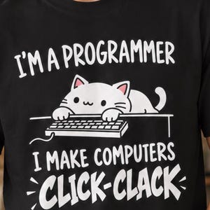 Könnte beinhalten: Ein schwarzes Kurzarm-T-Shirt mit einer weißen Grafik eines Katzenmotivs an einer Computertastatur. Der Text lautet: I'M A PROGRAMMER I MAKE COMPUTERS CLICK-CLACK. Das Design zeigt eine weiße Katze mit den Pfoten auf einer Tastatur.