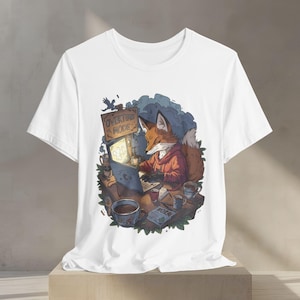 Könnte beinhalten: Ein weißes Kurzarm-T-Shirt mit einer grafischen Illustration eines Fuchses in einem roten Kapuzenpullover, der an einem Schreibtisch mit einem Laptop, mehreren Kaffeetassen und einem Schild mit der Aufschrift OVERTIME MODE sitzt.