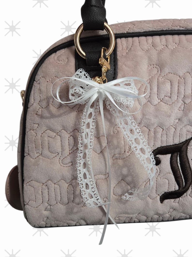 Puede incluir: Un bolso de mano rosa claro con asa negra y herrajes dorados. El bolso presenta un lazo de encaje blanco y una letra bordada marr&oacute;n. El bolso tiene un patr&oacute;n acolchado.