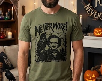 Puede incluir: Una camiseta de manga corta color verde oliva con un estampado gráfico negro de Edgar Allan Poe con un cuervo posado en su hombro. El texto "NEVERMORE!" está impreso en una fuente negra estilizada sobre la ilustración del autor.