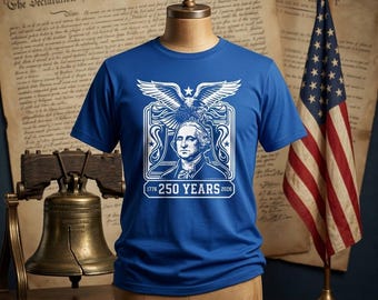 Puede incluir: Una camiseta de manga corta color azul real con un estampado gráfico en blanco de George Washington, un águila calva y el texto 1776 250 YEARS 2026. El diseño está centrado en el pecho de la camiseta, exhibida sobre un torso de maniquí.