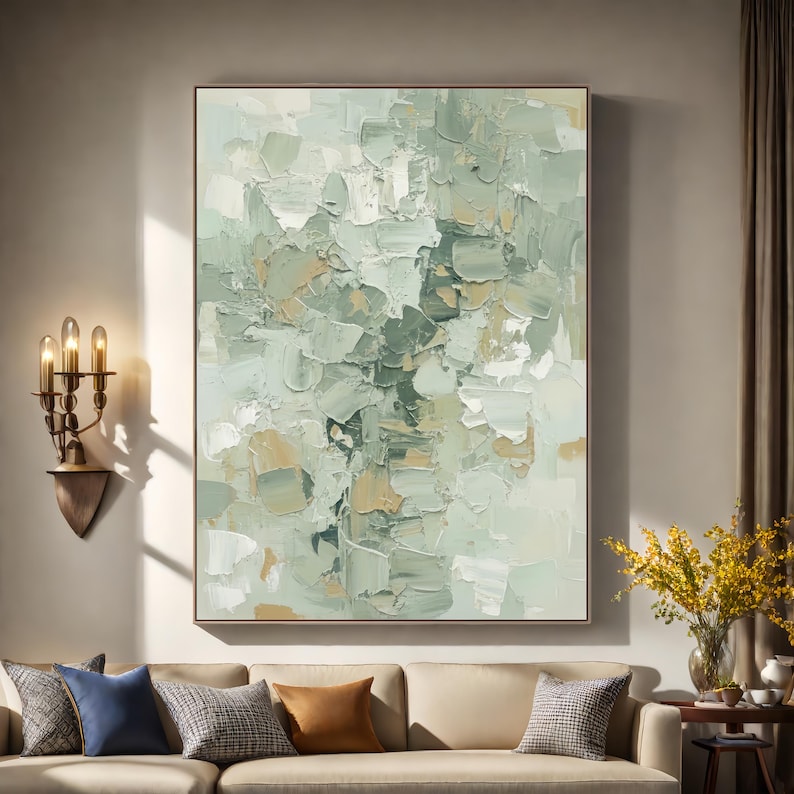 May include: Abstract oil painting with a neutral colour palette. The artwork features textured brushstrokes in shades of green, beige, and white, creating a layered effect. The painting is framed and displayed above a beige sofa with decorative cushions.
