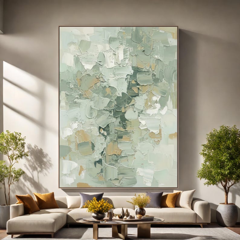 May include: Large abstract painting with a textured, impasto style. The artwork features a palette of soft greens, whites, and beige tones, creating a calming and modern aesthetic. The painting is framed and hangs above a cream-coloured sectional sofa.