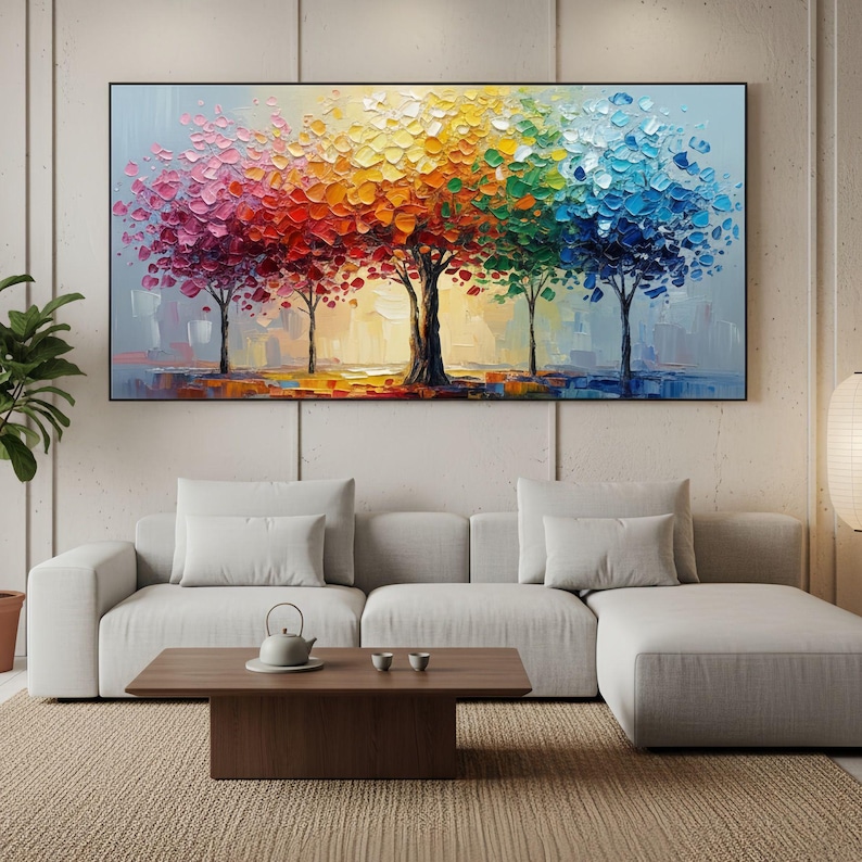 May include: A large, rectangular oil painting depicts five trees with vibrant, textured foliage in a spectrum of colors. The artwork features a black frame and is displayed above a white sectional sofa and a wooden coffee table.