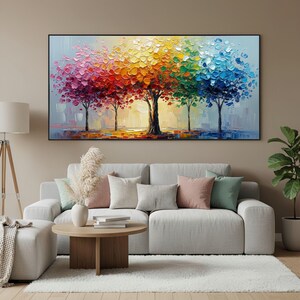 May include: A vibrant oil painting of five trees with colorful, textured foliage. The leaves transition from pink to red, orange, yellow, green, and blue. The artwork is displayed above a gray sofa with decorative pillows, enhancing the room's decor.