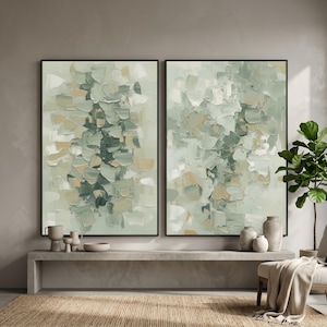 May include: Two framed abstract paintings with a textured, layered appearance. The artwork features a palette of muted greens, beige, and white, creating a soft, natural aesthetic. The paintings are displayed above a concrete bench with decorative vases.