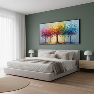 May include: A large, rectangular canvas art piece depicting a row of trees with vibrant, textured, rainbow-colored foliage. The artwork hangs above a bed with a white comforter and neutral-toned pillows. The room has a modern aesthetic.