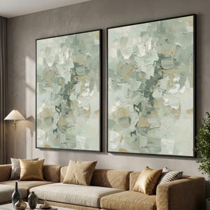 May include: Two framed abstract paintings with a textured, impasto style. The artwork features a palette of soft greens, creams, and beige, creating a calming aesthetic. The black frames add a modern touch to the wall art.