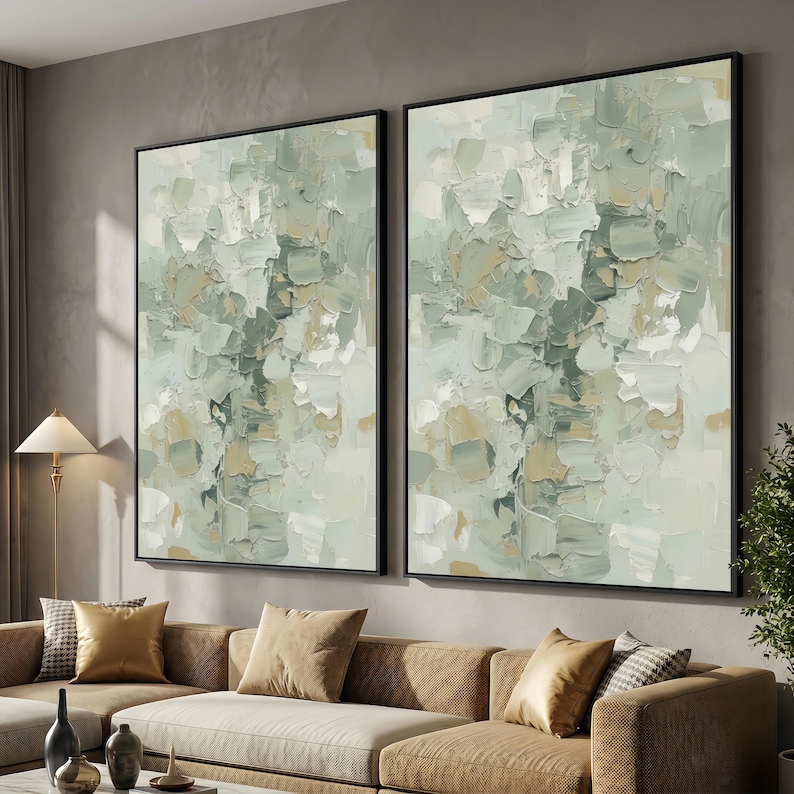 May include: Two framed abstract paintings with a textured, impasto style. The artwork features a palette of soft greens, creams, and beige, creating a calming aesthetic. The black frames add a modern touch to the wall art.