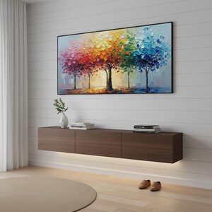 May include: A colorful abstract painting of trees with vibrant red, orange, yellow, green, and blue foliage hangs above a dark brown floating media console. The console has three sections and is illuminated by a strip of light.