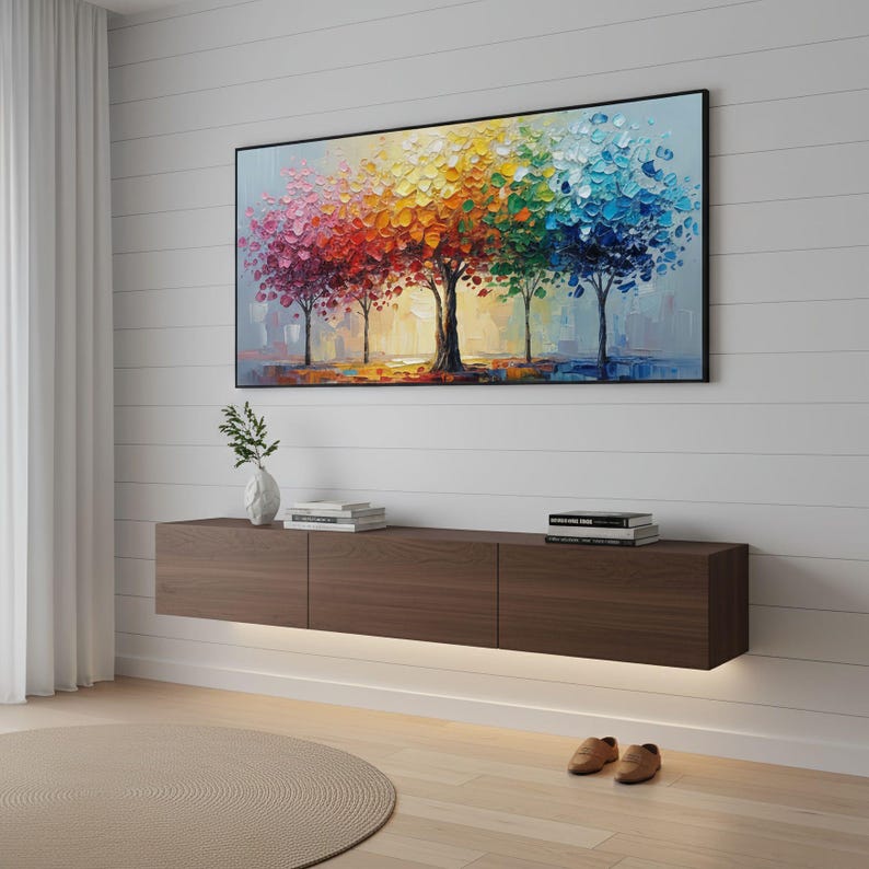 May include: A colorful abstract painting of trees with vibrant red, orange, yellow, green, and blue foliage hangs above a dark brown floating media console. The console has three sections and is illuminated by a strip of light.