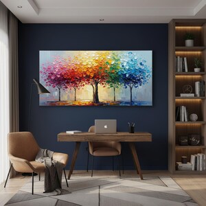 May include: A vibrant oil painting depicts five trees with colorful, textured foliage. The artwork features a spectrum of colors, from pink to blue, creating a rainbow effect. The painting is displayed above a wooden desk in a home office setting.