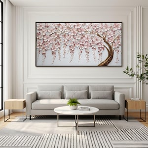 Könnte beinhalten: Gerahmtes Wandkunstwerk mit einem 3D-Relief eines Baumes mit rosa Blüten und herabfallenden Blumen. Der Baumstamm ist goldfarben strukturiert, vor einem hellgrauen Hintergrund. Das Kunstwerk wird über einem grauen Sofa präsentiert.