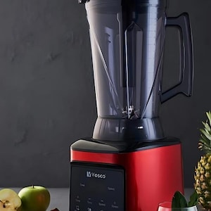 Könnte beinhalten: Ein roter und schwarzer Mixer mit einem transparenten Behälter, der über ein digitales Bedienfeld verfügt. Der Mixer steht neben frischem Obst und einem Glas grünen Saft, was auf gesunde Ernährung und die Zubereitung von Speisen hindeutet.