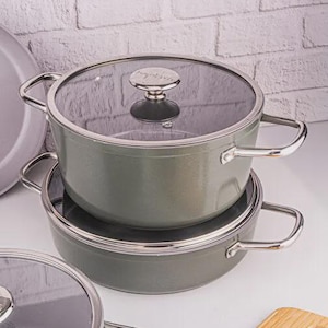 Könnte beinhalten: Ein Set aus zwei grauen Kochtöpfen mit Glasdeckeln und silbernen Griffen. Die Töpfe sind übereinander gestapelt. Die Deckel haben silberne Knöpfe. Ein Holzschneidebrett befindet sich im Hintergrund.