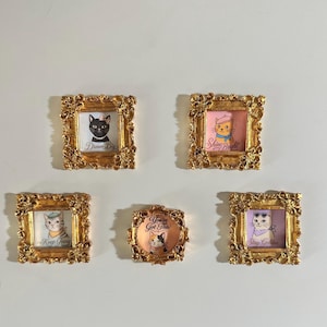 May include: Five framed cat portraits with gold ornate frames. Each frame features a different cat illustration with text: "Dream Big", "Shine Bright", "Keep Going", "You've Got This", and "Stay Golden". The cat illustrations have different accessories.