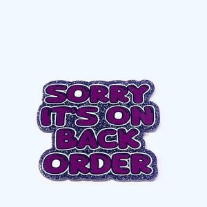 Könnte beinhalten: Ein lila-weiß glitzernder Anstecker mit dem Text "SORRY IT'S ON BACK ORDER" in einer fetten, blasenartigen Schriftart. Der Anstecker hat einen dunkelblauen Rand und eine weiße Umrandung.