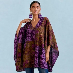 May include: A loose-fitting poncho top featuring a patchwork design of deep purple and olive green floral patterns. The garment has a V-neckline and wide, flowing sleeves. The fabric displays a repeating botanical print throughout the entire piece.
