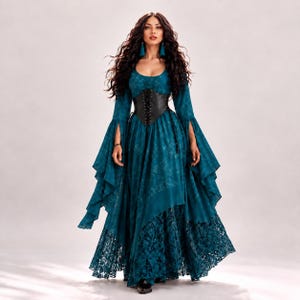 Puede incluir: Un vestido largo de color verde azulado con mangas largas acampanadas con aberturas, escote redondo y un cinturón tipo corsé negro con cordones. La falda tiene un diseño en capas con una sección superior lisa y un dobladillo de encaje oscuro.