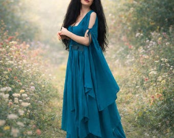 May include: A floor-length teal dress featuring a scoop neckline, cold-shoulder cutouts with tie details, and a layered, flowing skirt. The garment has a fitted bodice with a wide waistband and long, loose sleeves that drape down the sides.