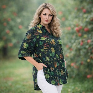 Puede incluir: Una camisa verde oscuro con un vibrante estampado floral de hojas verdes, amarillas y rojas. La camisa tiene mangas tres cuartos y se combina con pantalones blancos. La modelo está en un jardín.