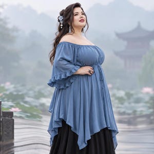 May include: A dusty blue off-the-shoulder blouse featuring a gathered neckline, ruffled elbow-length sleeves, and a drawstring waist. The garment has a handkerchief hemline that falls over a long, solid black skirt, creating a layered silhouette.