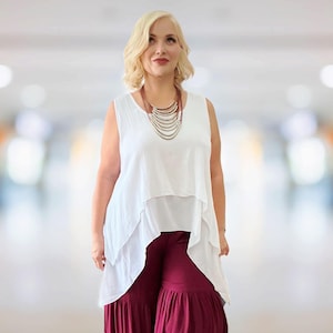 May include: A woman wearing a white sleeveless top with a layered design, paired with burgundy palazzo pants. A multi-strand necklace adds a touch of elegance. The outfit is suitable for casual or semi-formal occasions.