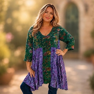 Pode incluir: Uma túnica verde e roxa com decote em V e mangas três quartos. A parte superior apresenta um padrão floral em tons de vermelho, amarelo e verde. A parte inferior é roxa vibrante com um design floral semelhante. A modelo usa jeans azuis.