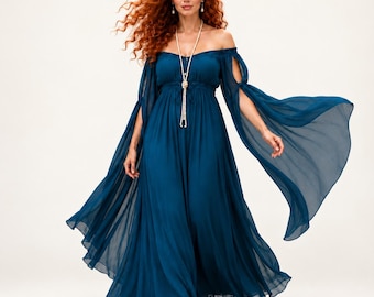 Puede incluir: Un vestido largo hasta el suelo de color verde azulado con hombros descubiertos, mangas largas y fluidas con aberturas y un corpiño fruncido. La prenda se combina con un collar largo de perlas de varias hebras que cae por el pecho.